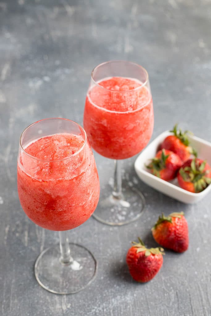 two glasses of frozen rose next to a bowl of strawberries