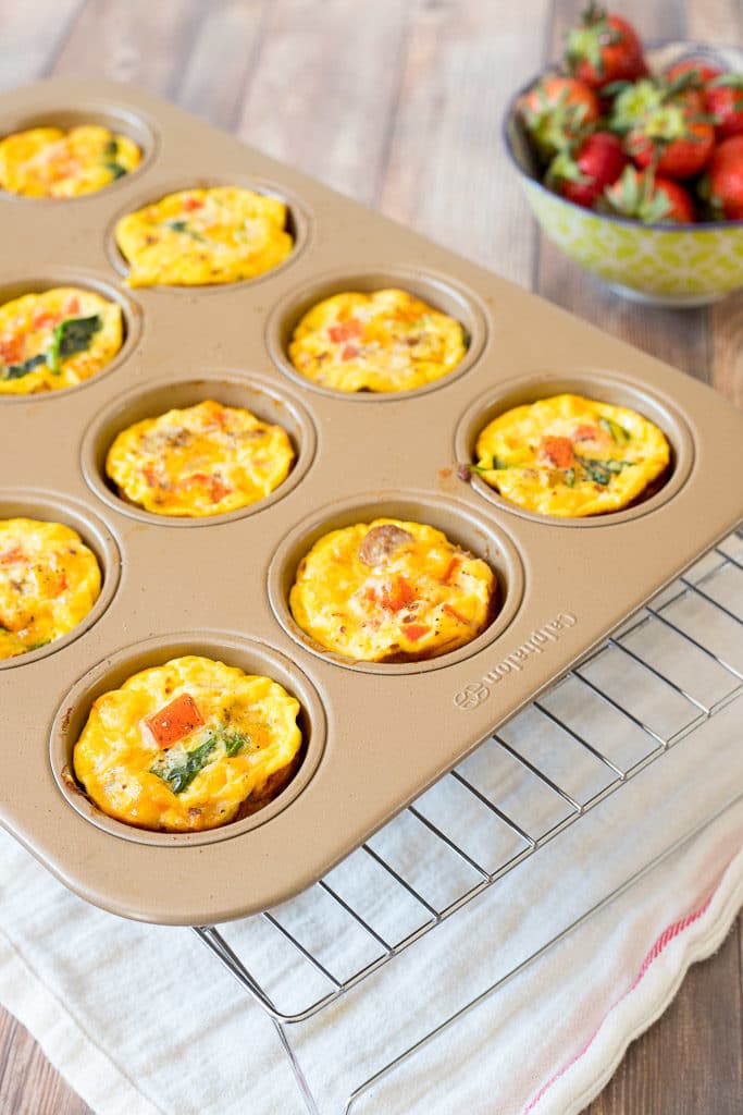 egg bake muffins in a pan next to a bowl of strawberries